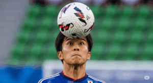 日本人サッカー選手が、目を開けて、おでこの一番硬い部分でボールをミートしている瞬間のクローズアップ写真。