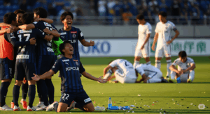 J2の試合終了後、勝利して歓喜する選手たちと、敗れてピッチに崩れ落ちる選手たちが対照的に写っている写真。